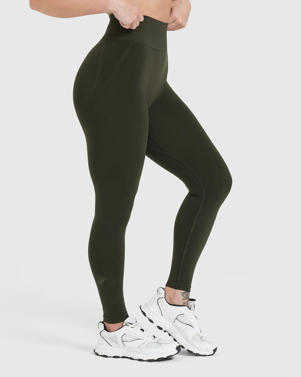 Person wearing olive green leggings and white sneakers on a white background